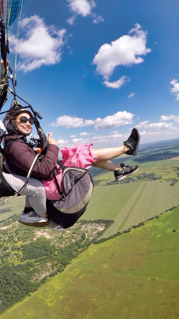 Человек в воздухе с восторженной улыбкой, держащийся за стропы параплана.